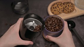 Close up. Woman's hands pour coffee beans into a coffee grinder from a transparent glass. Oatmeal cookies on a wooden board, black spoon. Coffee preparation. Dark background - Powered by Shutterstock - Get 15% off with code: PIKWIZARD15