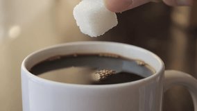 Slow Motion Hand Dropping Sugar Cube Into Black Coffee. Sugar Falling Down Into Coffee Cup. Coffee Caffeine Addiction Junk Food. Concept of Unhealthy Eating, Diabetes, Obesity, Heart Disease.  - Powered by Shutterstock - Get 15% off with code: PIKWIZARD15