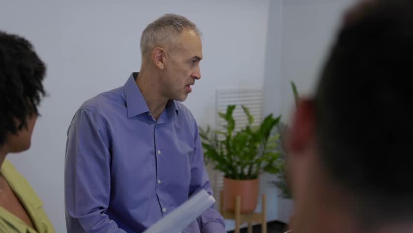 Middle-aged business man leading group conversation with his team. Coworkers engage in a collaborative discussion guided by their workplace leader. Business and teamwork concept.
