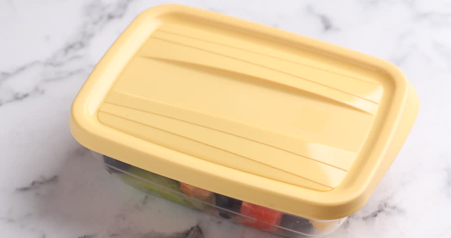 Woman opening plastic container with tasty fruit salad at white marble table, closeup. Healthy snack