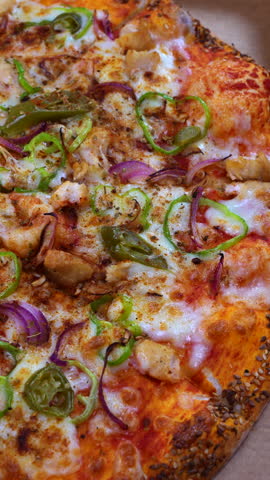 Rotating close up of a hot pizza with melted cheese, chicken, peppers, onions and a sesame crust. A clear detailed view of the toppings on the spinning surface.