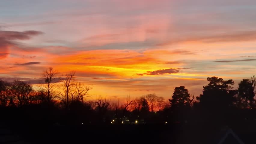 Saffron Walden, Essex, UK - February 01, 2024: Beautiful sunset with saturated orange, red, and yellows caused by Sahara dust in the atmosphere with silhouetted trees.