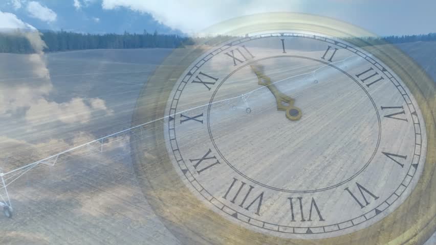 Antique clock face rotating over tilled field on drone pan, clouds shifting, showing time passing. Timepiece, aerial, farmland, irrigation, pivot, vintage, timelapse