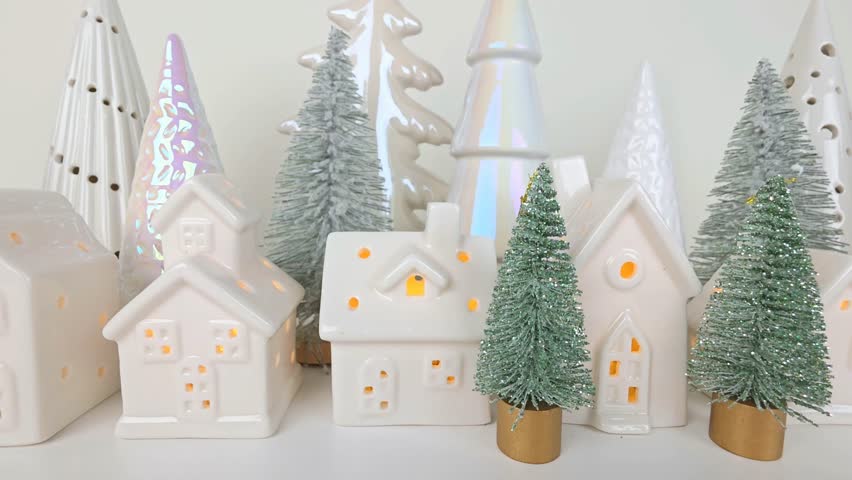 Tiny Christmas village with lit white houses and tree decor on a white shelf. Slow zoom out motion.
