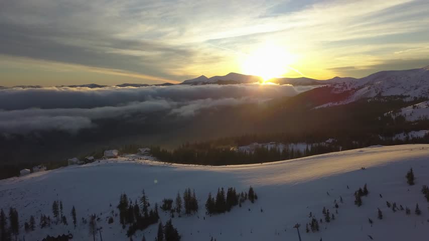 Sunset over snowy mountain range with low-lying clouds in the valley