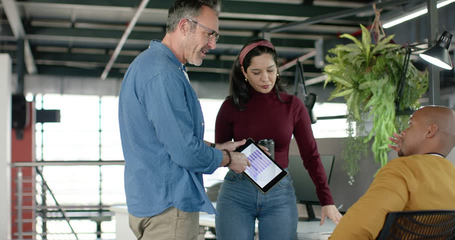 Diverse colleagues approaching workstation collaborating over tablet showing chart to review data. Collaboration, teamwork, business, analytics, communication, modern, professional