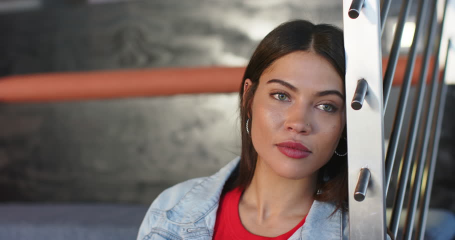 Indian woman resting against railing gazing off camera and smiling into lens in lounge, copy space. Contemplative, relaxed, candid, warm, modern, youthful, approachable