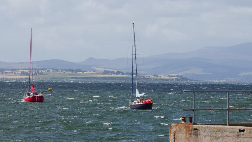 Two sailboats move across choppy Cromarty Firth, Scotland, under bright daylight with steady camera