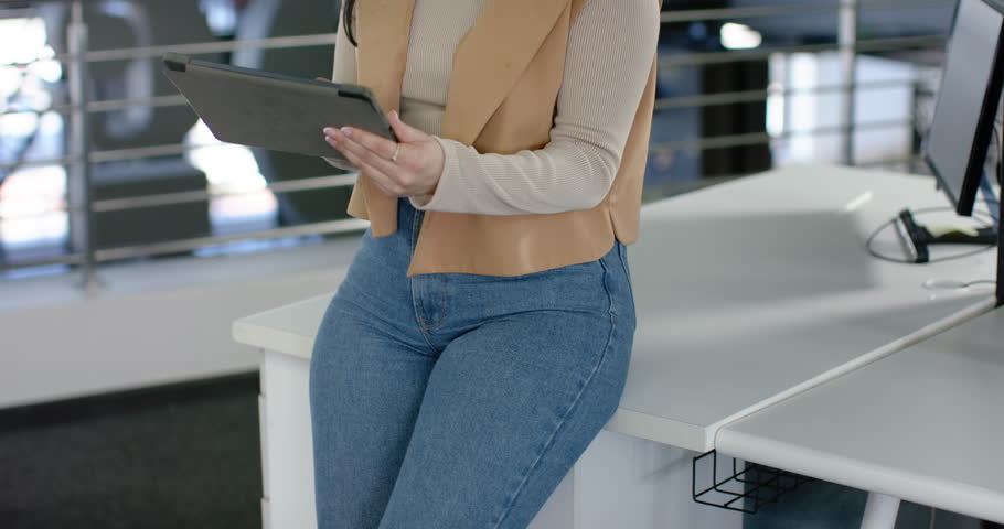 Mid adult Hispanic woman tapping tablet and swiping files at white office desk while reviewing info. Professional, workspace, modern, technology, focus, concentration, productivity