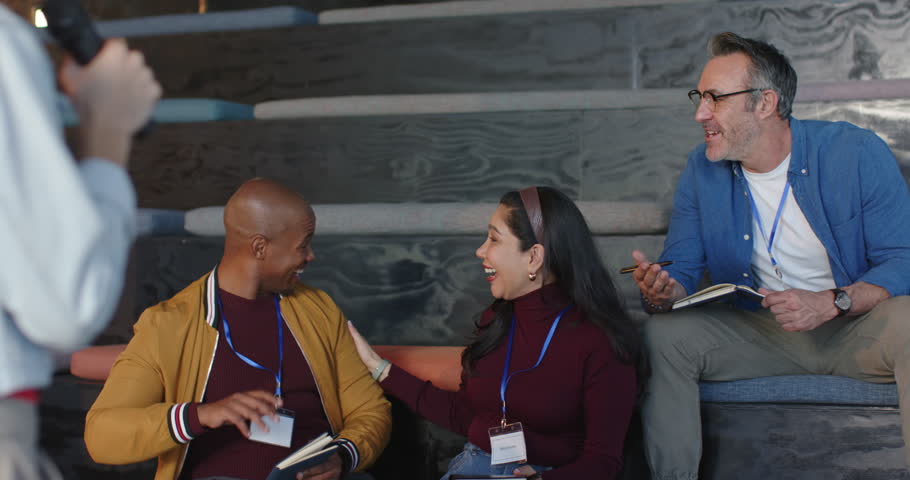 Diverse colleagues glancing at speaker's point then high-fiving and holding notebooks on benches. Collaboration, camaraderie, networking, professional, cheerful, dynamic, engagement
