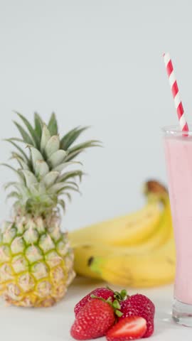 Hand adds striped straw and strawberry garnish to pink smoothie in glass, bright studio lighting.