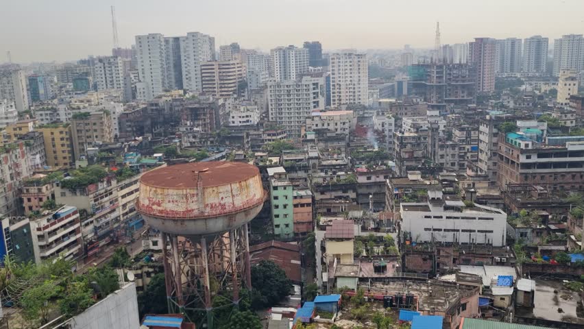 View from a high-rise building over Dhaka, Bangladesh, revealing a dense urban jungle of mixed-height buildings stretching into the distance under a hazy, smog-filled grey sky