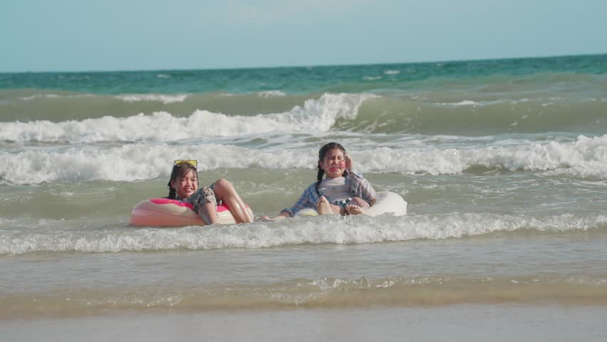 Two happy little girls floating in inflatable ring playing splashing water in the sea waves together. Two children having a joyful time at the beach. Leisure enjoying the weekend concept