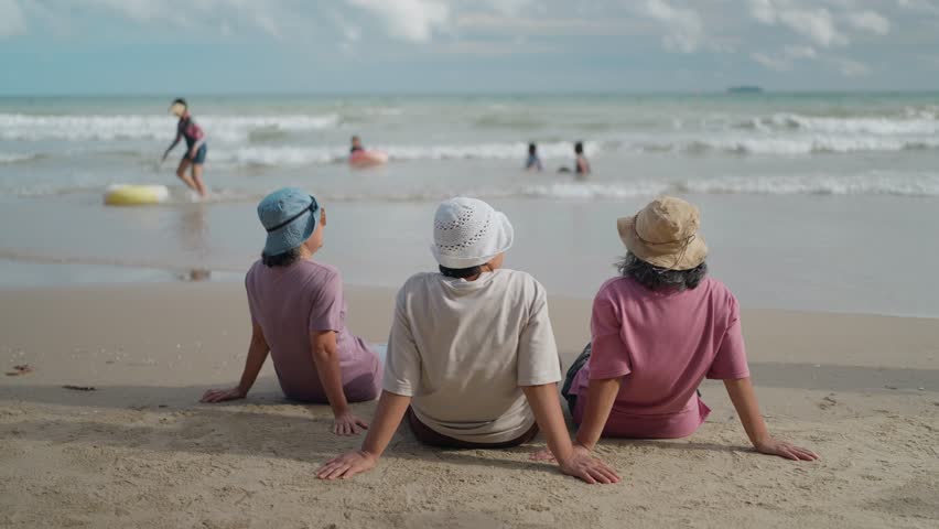 A group of mothers sitting on the beach, relaxing, and engaging in conversation while keeping a watchful eye on their children playing safely in the ocean water