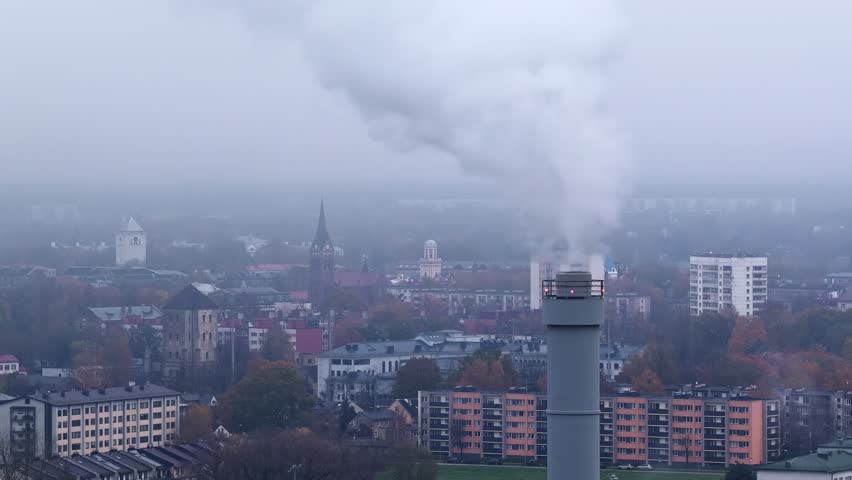 Drone smoke plume rising from industrial factory chimney surrounded by rural buildings below