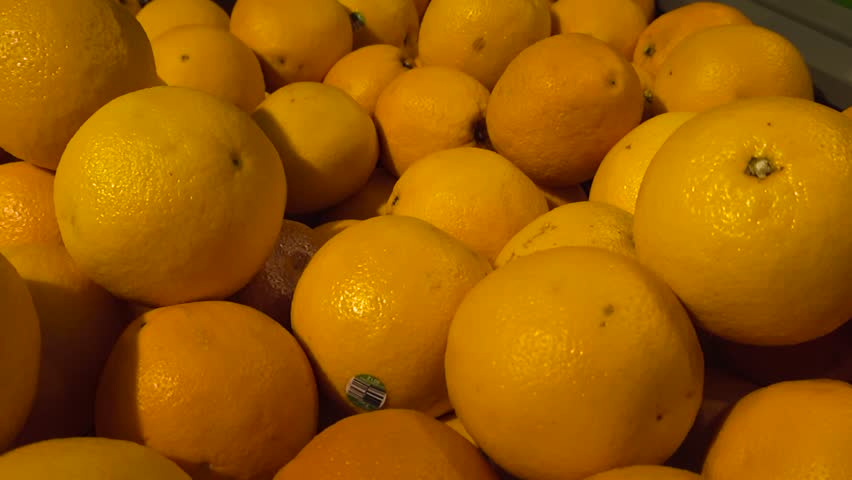 Low angle slow motion gliding over large piles of fresh oranges stacked in market stall in closeup. Fruits layered on top of each other, capturing rich texture. Background tangerines in shallow depth