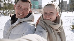 Caucasian couple smiles at camera during selfie against backdrop of sunny winter holiday cityscape. Portrait of man and woman are recording video message while traveling. - Powered by Shutterstock - Get 15% off with code: PIKWIZARD15