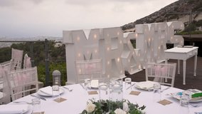 A stunning wedding reception is arranged outdoors with a breathtaking mountain view. The table is set with white decorations, flowers, and illuminated letters declaring Mr and Mrs. - Powered by Shutterstock - Get 15% off with code: PIKWIZARD15