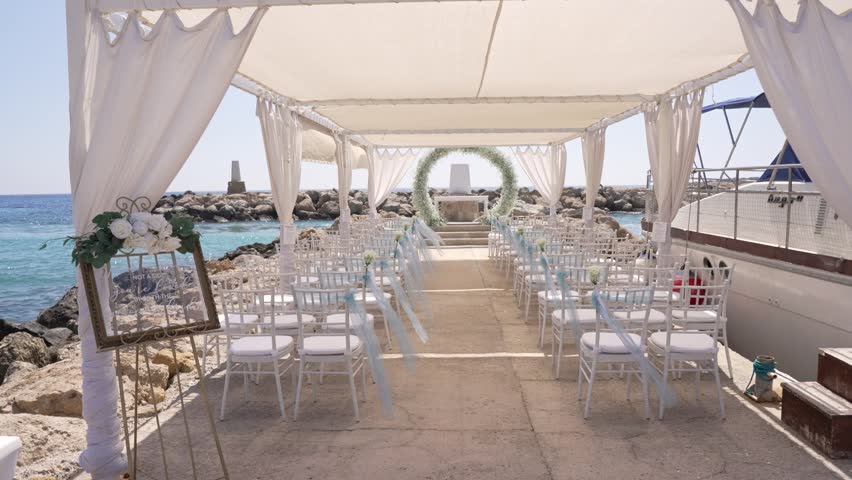 A lovely wedding ceremony is arranged by the beach with white chairs and floral decorations. Guests will soon arrive to enjoy this special event near the water.
