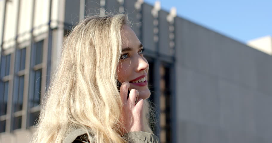 Woman receiving call on smartphone standing on city sidewalk looking up smiling and laughing. Urban, contemporary, casual, communications, lifestyle, vibrant, optimistic