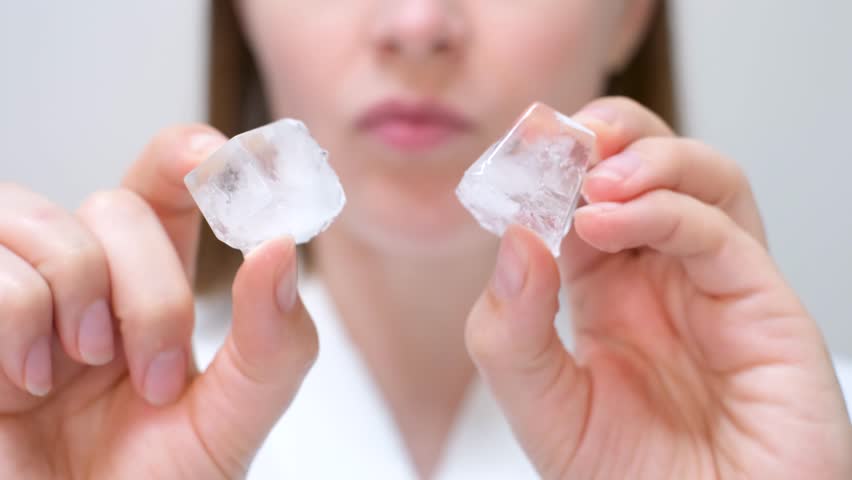 Young woman holding ice cube on face background, skin care concept.