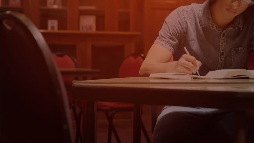 Man studying in library with HUD appearing, pulsing over open book while occluding view, writing. Study, paneling, shelves, notebook, pen, glasses, warmth