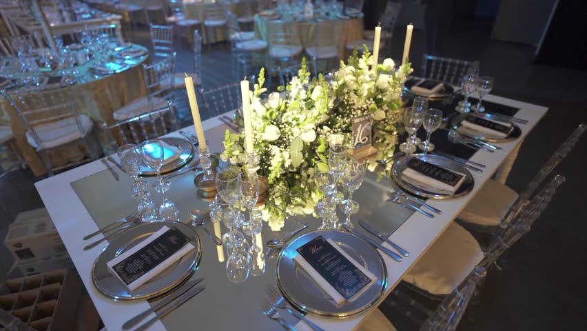 Elegant luxurious banquet table setup with silver plates and crystal glasses in hall.
