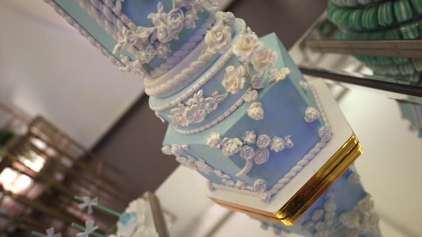An upward camera motion reveals a tall tiered wedding cake in pastel blue with white floral and scrollwork icing, showcasing intricate craftsmanship and elegance in a formal banquet setting.