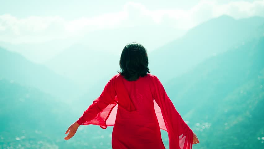 4K shot of Indian teenager girl raise hands, wearing traditional Indian salwar suite And dupatta fluttering in wind. Tourist standing against mountains in Manali, Himachal Pradesh, India.
