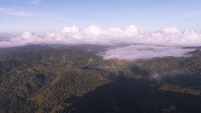 Epic wide aerial shot of a massive layer of cumulus clouds and low fog hovering above a dense, dark tropical forest and hilly terrain. Captured during the beautiful, serene light of sunrise or sunset. - Powered by Shutterstock - Get 15% off with code: PIKWIZARD15