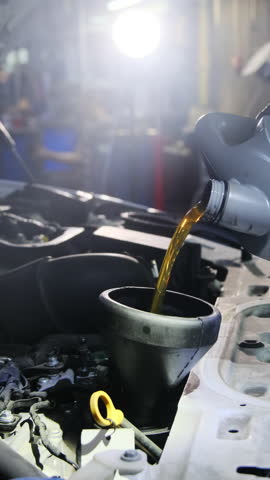 Mechanic pours liquid into special small container in car. Master changes engine oil during vehicle maintenance in spacious service center