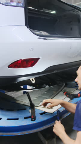 Mechanic works on restoring lower part of vehicle under trunk. Man with screwdriver examines surface of object and begins modification process