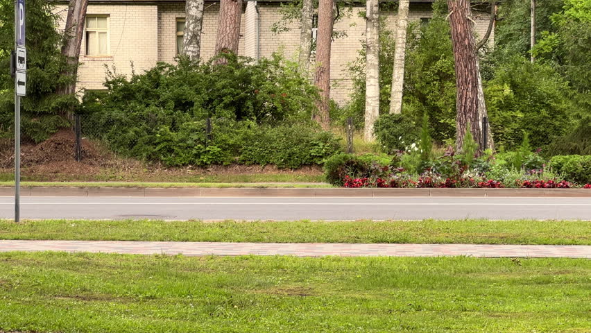 wide shot of a silver passenger wagon (estate car) driving fast on a multi-lane urban road. The car is blurred due to motion, highlighting speed and movement. Foreground shows green grass and sidewalk