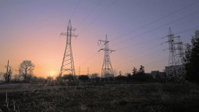 A low-angle shot showing a group of high-voltage transmission towers (pylons) as dark silhouettes. The vibrant sky features gradients of orange, pink, and purple, indicating sunset or sunrise - Powered by Shutterstock - Get 15% off with code: PIKWIZARD15