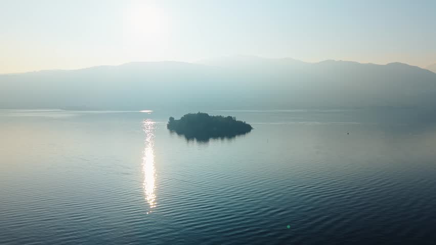 Aerial view of the lush Isola Madre island surrounded by the tranquil waters of Lake Maggiore, reflecting the sun's golden light, Isola Madre, Stresa, Italy.