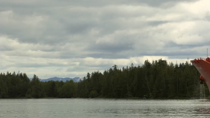 Serene view of Loch Long near Arrochar, Scotland, showing calm waters, forested Highlands, and the bow of a docked vessel beneath a cloudy sky.