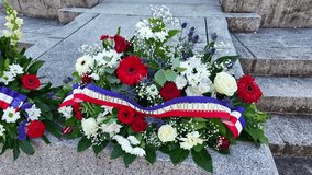 Red, white, and blue floral wreath with a MÉMOIRE MILITAIRE tricolor ribbon displayed on stone steps, symbolizing remembrance of fallen soldiers at French military or national commemoration ceremony. - Powered by Shutterstock - Get 15% off with code: PIKWIZARD15
