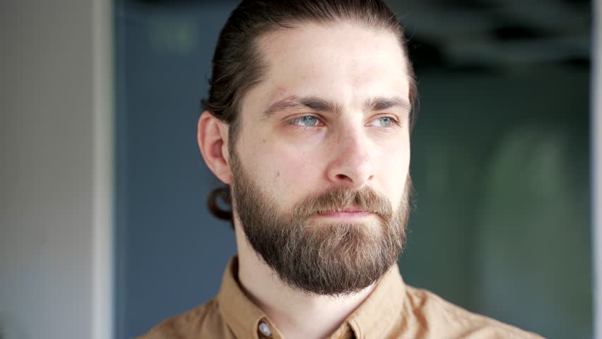 Close up portrait of smiling bearded businessman standing at workplace in modern business office. Head shot of happy successful entrepreneur looking at camera. Face of a cheerful handsome male worker