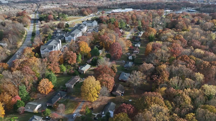 High-altitude drone footage showcasing a peaceful American suburban community nestled among vibrant autumn trees, winding roads, and neat houses under clear daytime skies