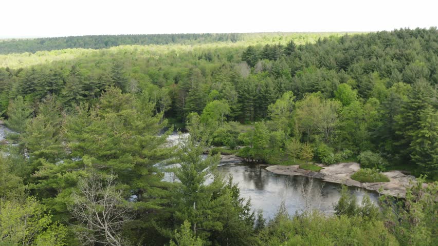 Aerial view over a wide river flowing down a rocky terrain, surrounded by a green mountain forest