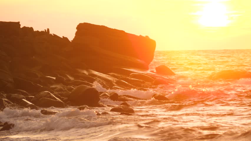 Sunset sun setting, ocean waves over shore stones cliff in Southeast Asia