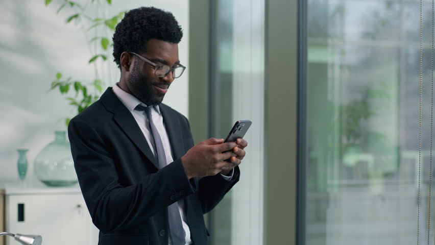 African American businessman smiling looking at smartphone in modern office happy male professional business man reading message using mobile phone digital communication success corporate workplace - Powered by Shutterstock - Get 15% off with code: PIKWIZARD15