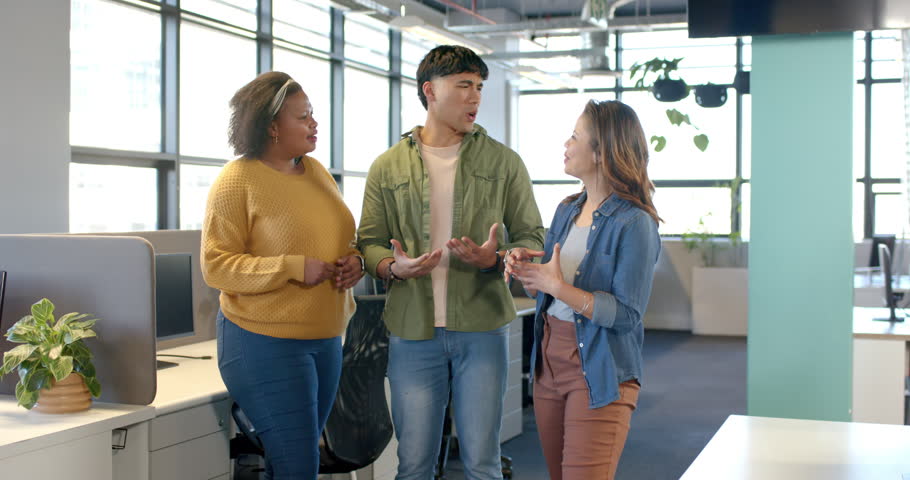 Diverse coworkers opening project talk beside desk partitions in open office, gesturing and smiling. Collaboration, teamwork, communication, modernity, professionalism, casual, positivity
