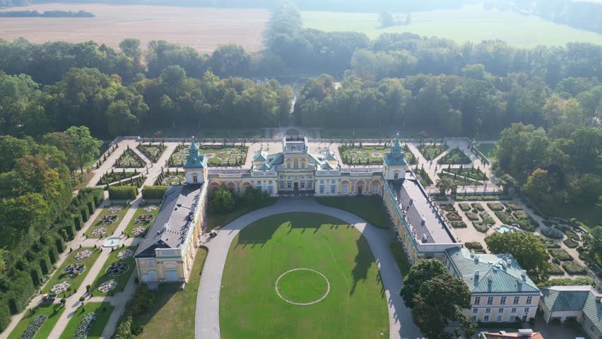 Stunning drone view of Wilanów Palace in Warsaw with ornate baroque facade, colorful roof, and vast landscaped gardens bathed in soft morning light.