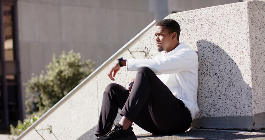 African American man shifting expression from thought to laughter upon camera gaze on rooftop. Contemplation, urban, skyline, casualwear, scenery, positive, relaxation