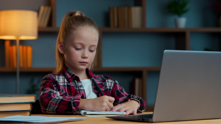 Caucasian concentrated daughter child kid girl studying online from home e-learning with laptop writing notes listening internet lesson class course study learn with computer focused write homework
