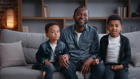 Happy African American family looking at camera at home carefree joyful father with two little sons boys kids children smiling pointing in front watching TV television cinema movie relaxing on sofa - Powered by Shutterstock - Get 15% off with code: PIKWIZARD15