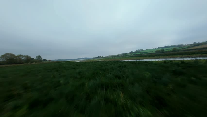 Aerial view of a serene river meandering through fields, the scene painted with earthy tones under an overcast sky, Uppingham, England, United Kingdom.