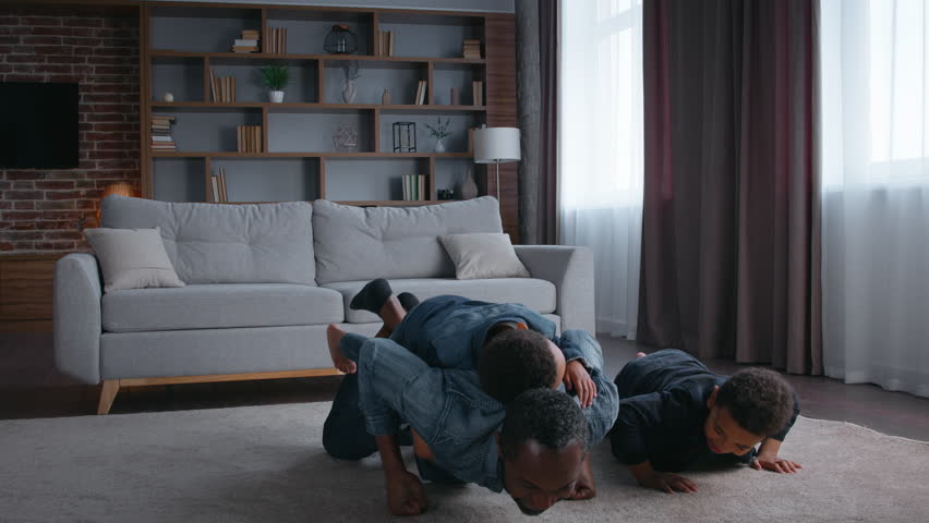 African American happy family pushing up father with sons push up together doing sport workout game at home two little boys kids children with dad teaching training exercise wellness healthy lifestyle