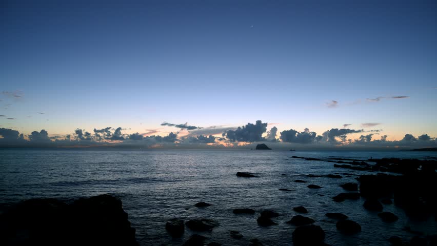 Stunning wide shot of crepuscular rays shooting into the blue and purple sky over the rocky coastline and ocean during pre sunrise in Wanli District New Taipei City Taiwan.